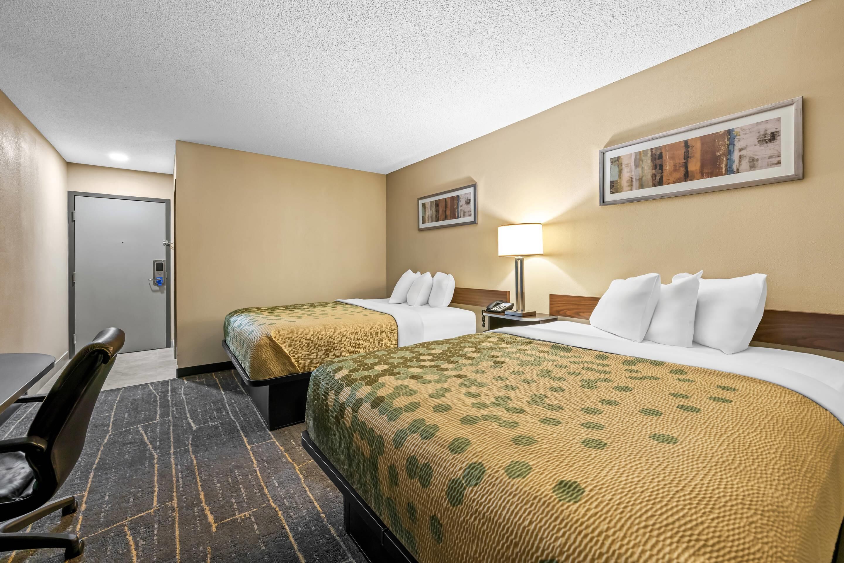 A hotel room with two beds, a desk, and a chair.