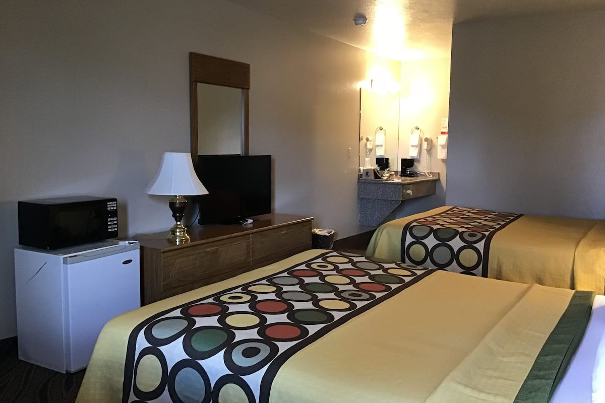 Une chambre d’hôtel avec deux lits, une télévision, un four à micro-ondes, une lampe, un miroir et un petit bureau avec un téléphone.