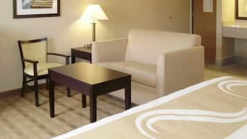 A hotel room with a sofa, a chair, a small table, a lamp, and a framed picture on the wall.