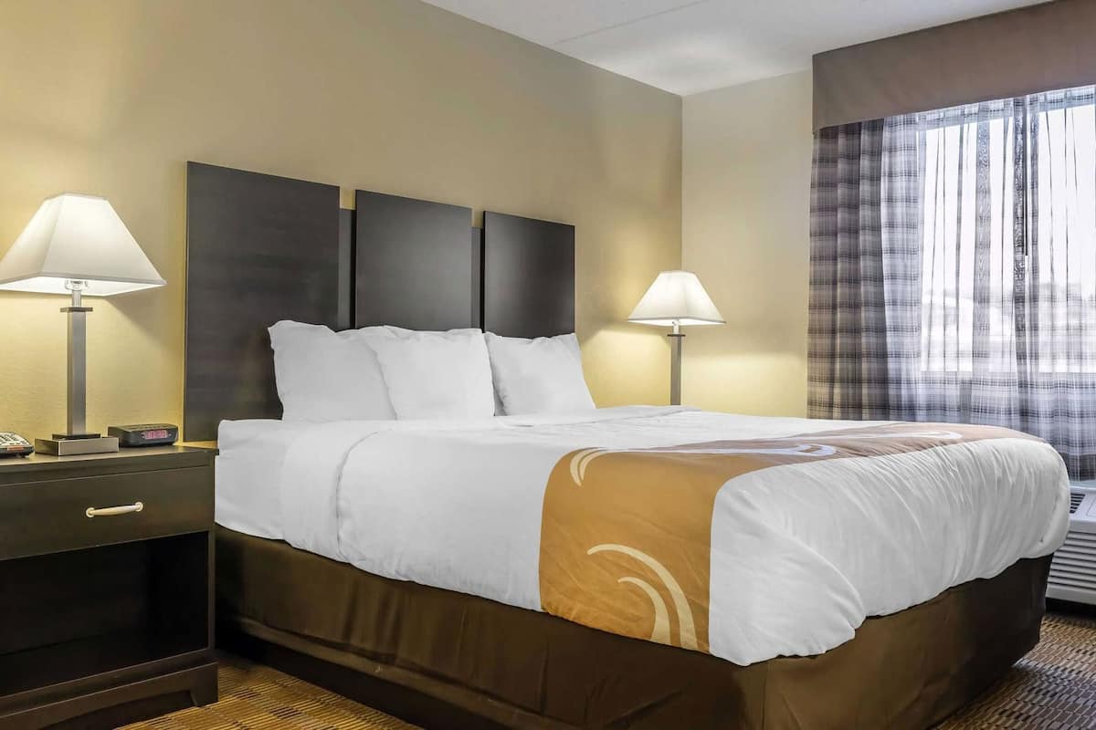 A hotel room with a bed, two bedside lamps, a nightstand, and a window with curtains.