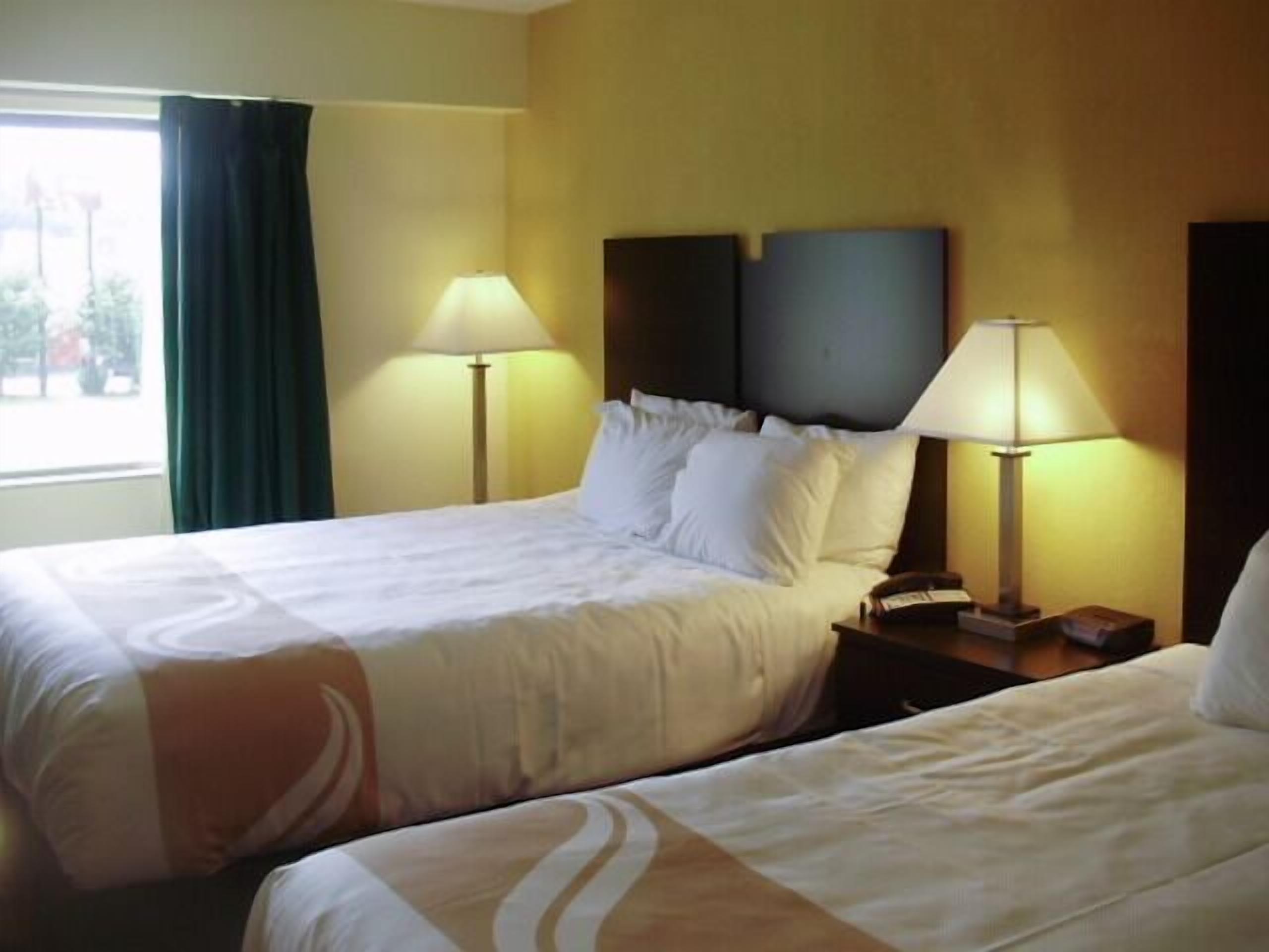 Une chambre d’hôtel avec deux lits, chacun doté de draps blancs et d’une tête de lit. Deux lampes de chevet sont posées sur des tables de chevet en bois.