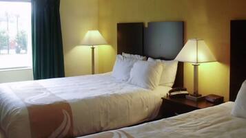 A hotel room with two beds, each with white linens and a headboard. There are two bedside lamps on wooden nightstands.