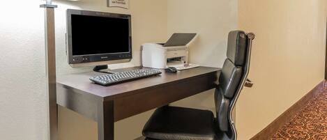 A hotel workspace with a desk, computer, printer, and a black office chair.