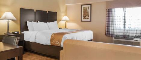 Habitación de hotel con cama, dos lámparas de noche, escritorio, silla, un cuadro en la pared y ventana con cortinas.