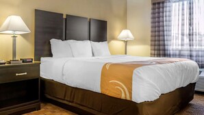 A hotel room with a large bed, two bedside tables with lamps, a headboard, and a window with curtains.