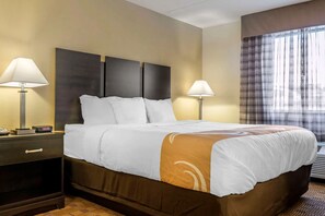 A hotel room with a large bed, two bedside tables with lamps, a headboard, and a window with curtains.
