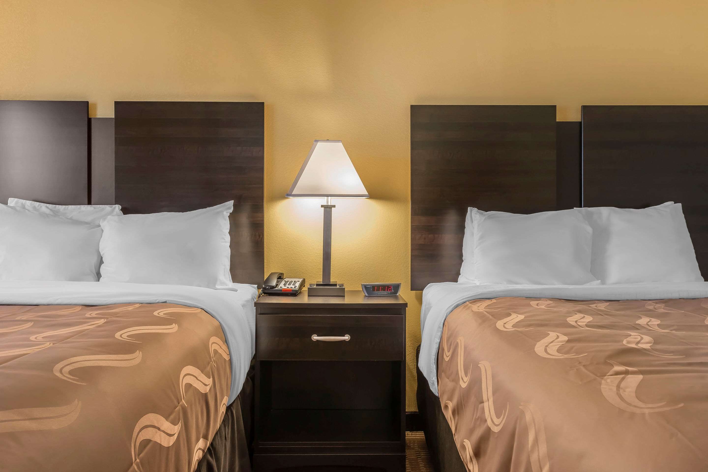 Een hotelkamer met twee bedden, een nachtkastje met een lamp, een telefoon en een klein tafeltje.