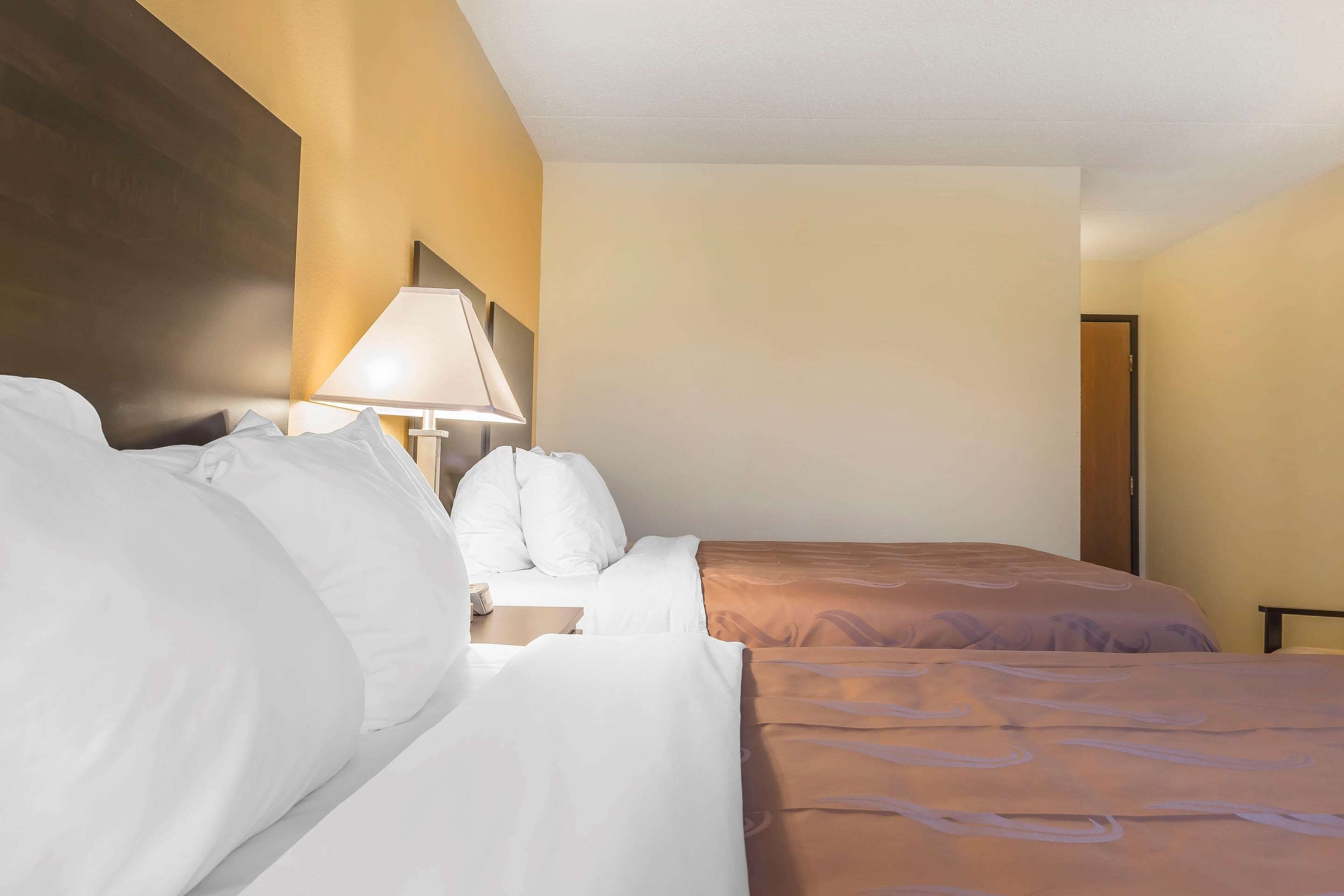 Una habitación de hotel con dos camas, una mesita de noche, una lámpara y una puerta.