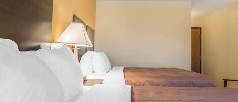Una habitación de hotel con dos camas, una mesita de noche, una lámpara y una puerta.
