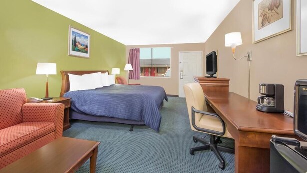 Habitación de hotel con cama, escritorio, silla, televisor y cafetera.