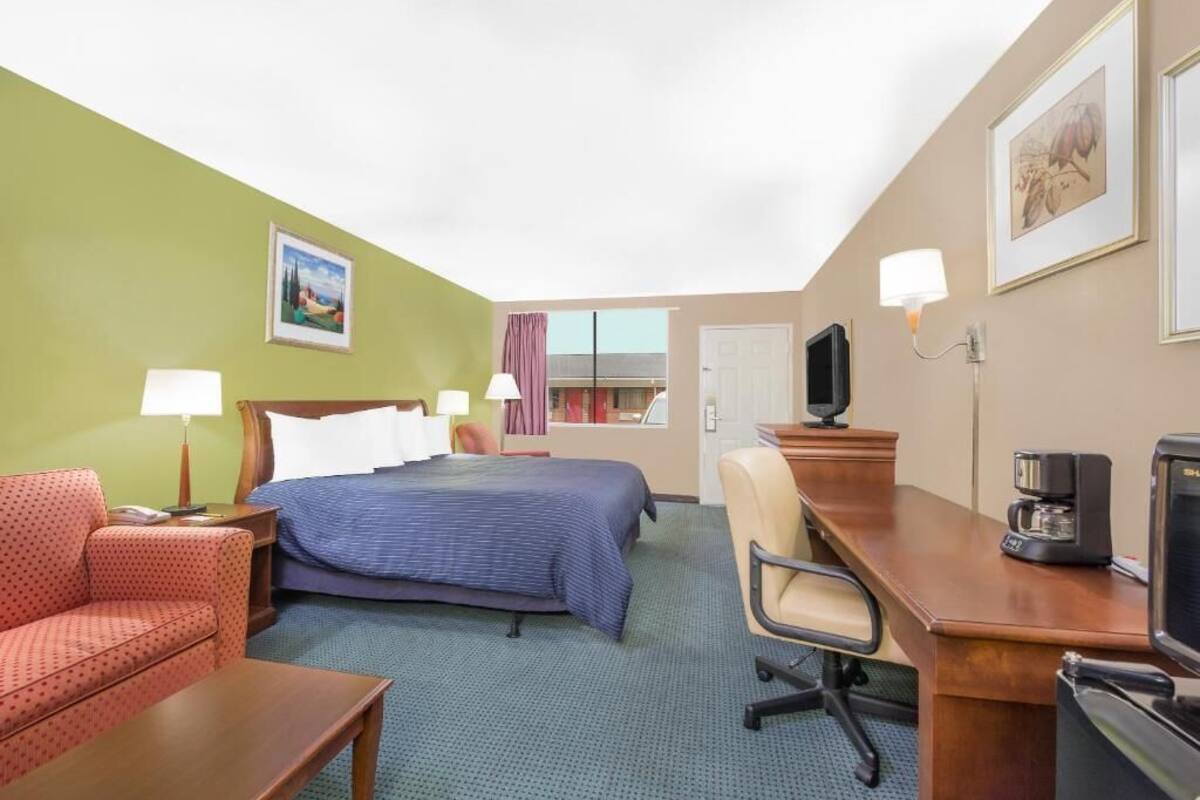 Habitación de hotel con cama, escritorio, silla, televisor y cafetera.