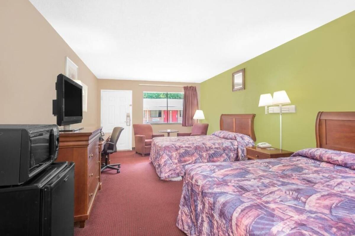 Una habitación de hotel con dos camas, un escritorio, una silla, un televisor y una lámpara.