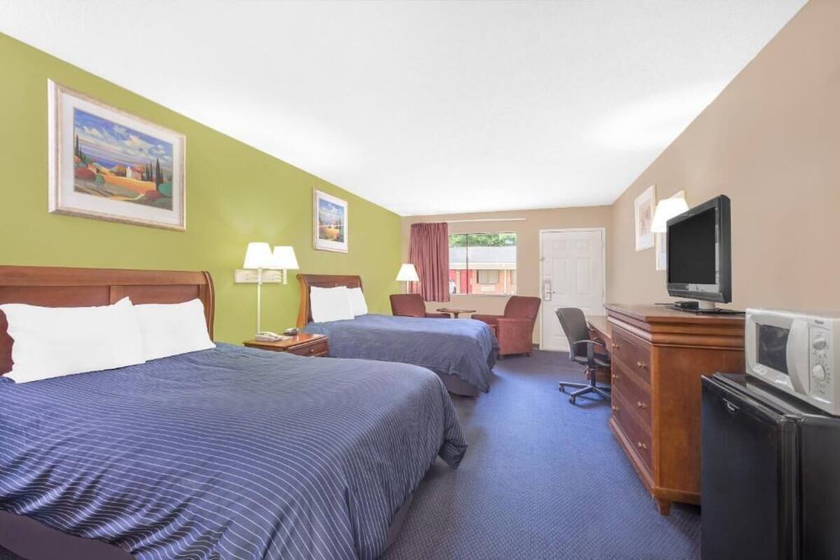 Una habitación de hotel con dos camas, un escritorio, una silla, un televisor y un aparador.