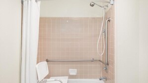 Zona de ducha con bañera blanca, barra de apoyo y cabezal de ducha.