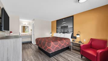 A hotel room with a bed, a desk, a chair, a desk lamp, a nightstand, and a wall-mounted TV.