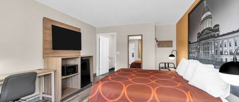 A hotel room with a bed, a desk, a television, a microwave, and a bathroom visible through an open door.