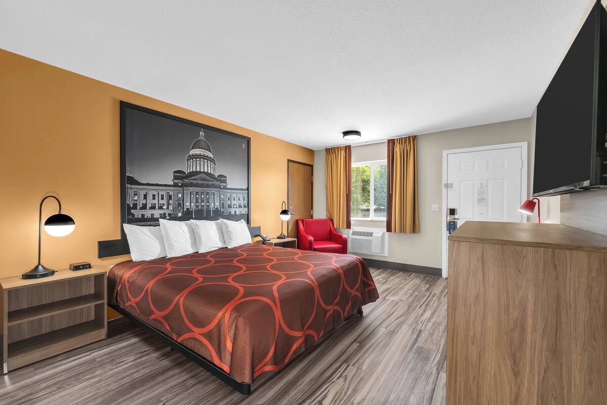 Habitación de hotel con cama, escritorio, silla, televisión y un amplio ventanal con cortinas.
