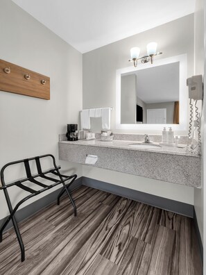 A modern bathroom with a granite countertop, a mirror with lights, a hairdryer, and a towel rack. - Super 8 by Wyndham Siloam Springs (Siloam Springs)