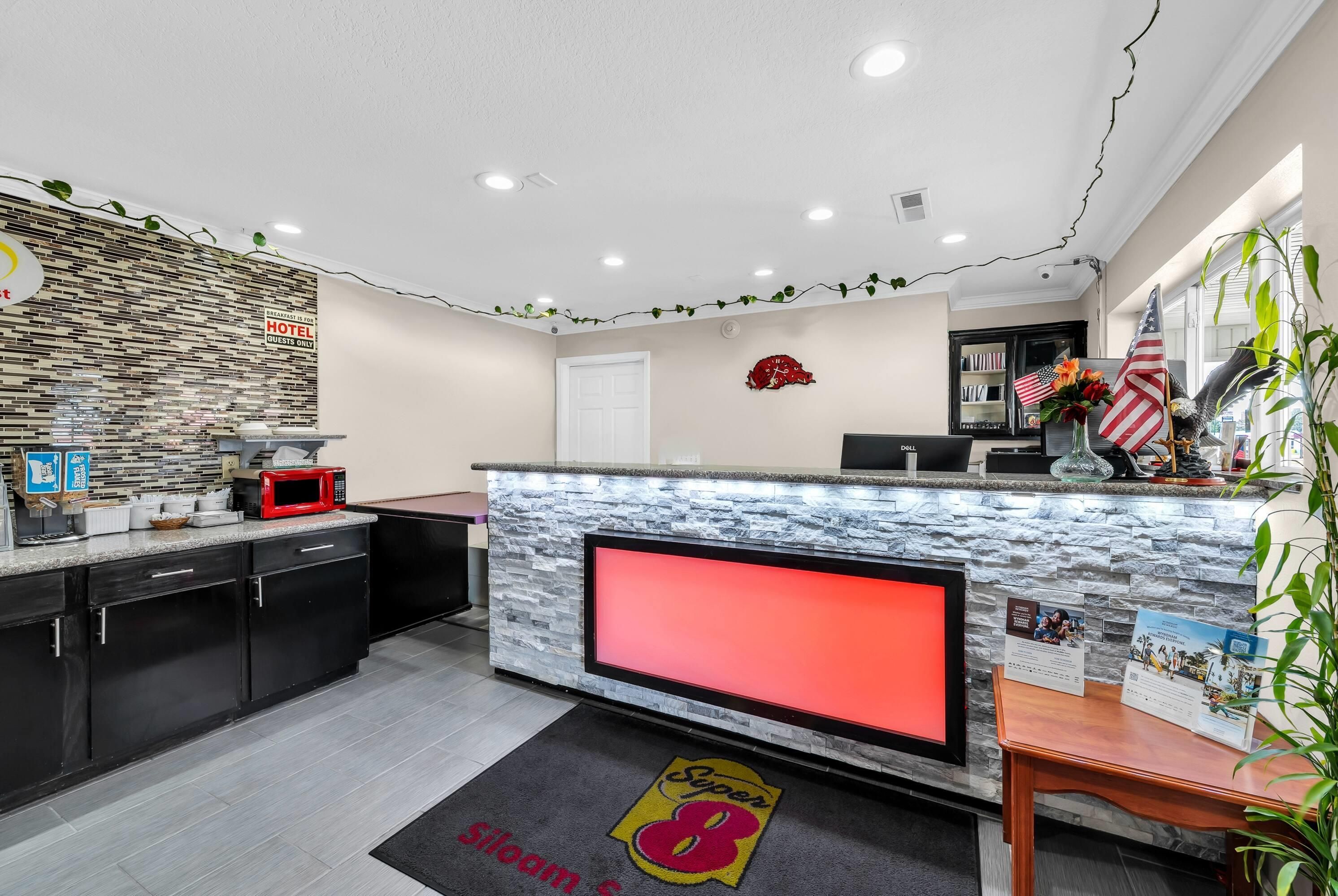 A hotel reception area with a stone counter, a flat-screen TV, and a red carpet with 'Super 8' branding.