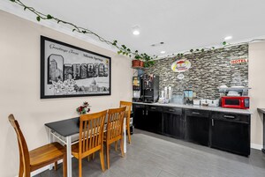 Una cocina de hotel con barra de desayuno, un cartel de bienvenida enmarcado y una máquina de café.