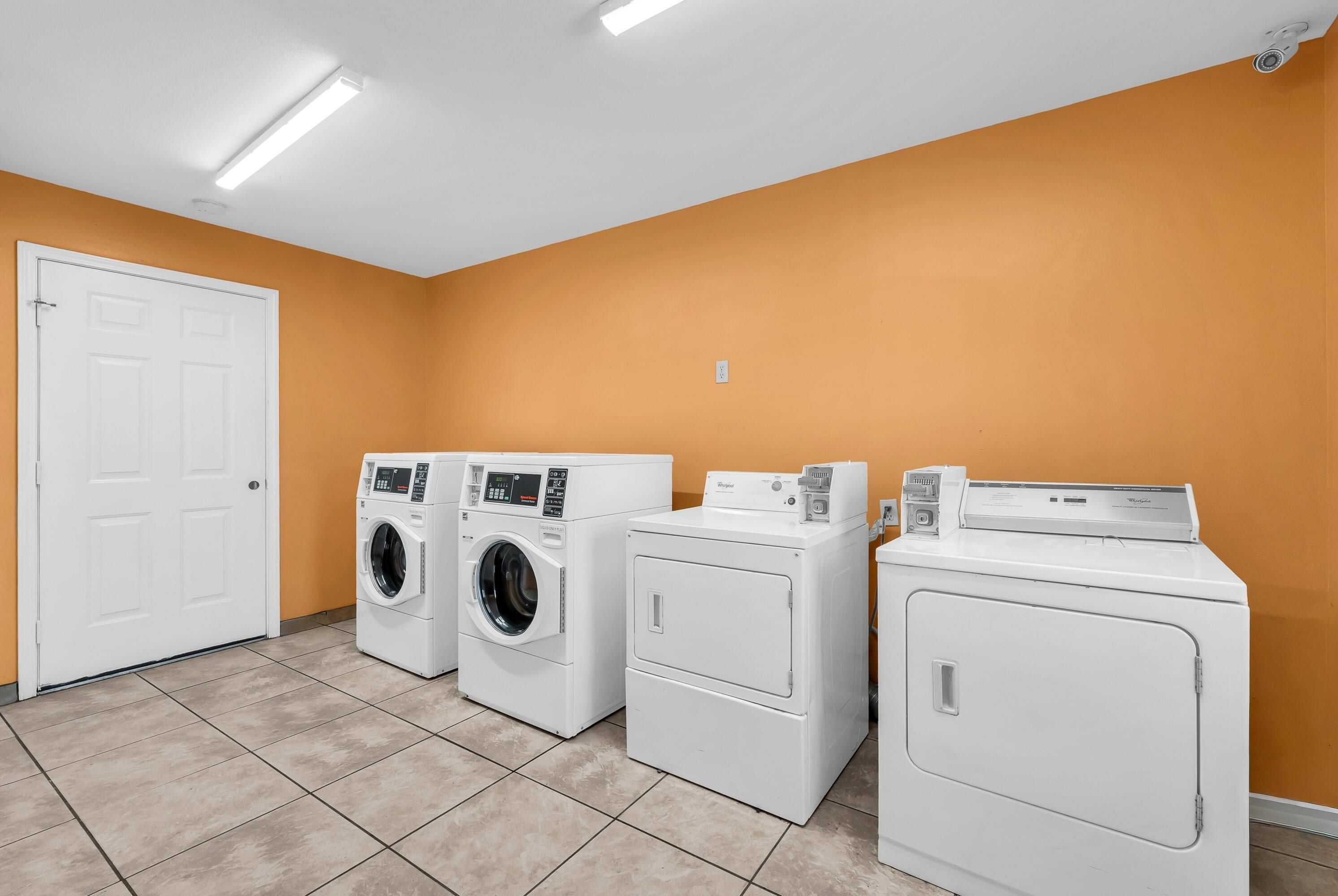 A laundry room with three washers and dryers, a white door, and orange walls.