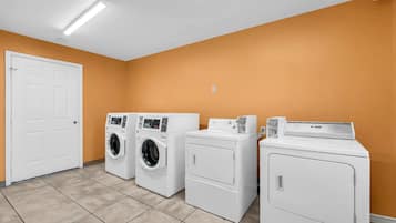 A laundry room with three washers and dryers, a white door, and orange walls.
