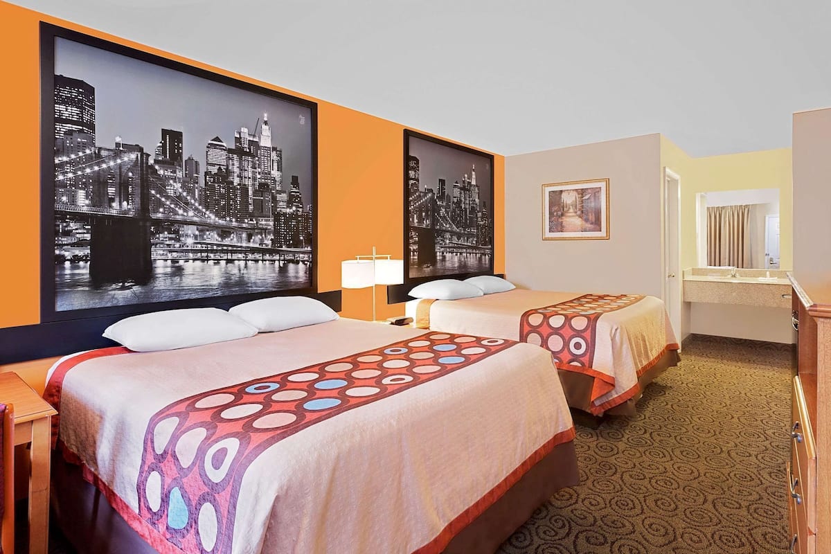 A hotel room with two beds, a television, a desk, and a bathroom visible through an open door.