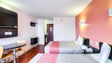Habitación de hotel con dos camas, un escritorio, una silla, un televisor y una puerta que da a un baño.