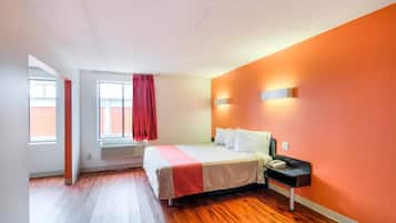 Una habitación de hotel con una cama, una mesita de noche con teléfono, una ventana con cortinas y una pared de acento roja.