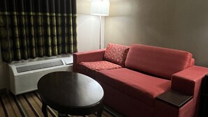 A hotel room with a red sofa, a small round table, a floor lamp, and a radiator.