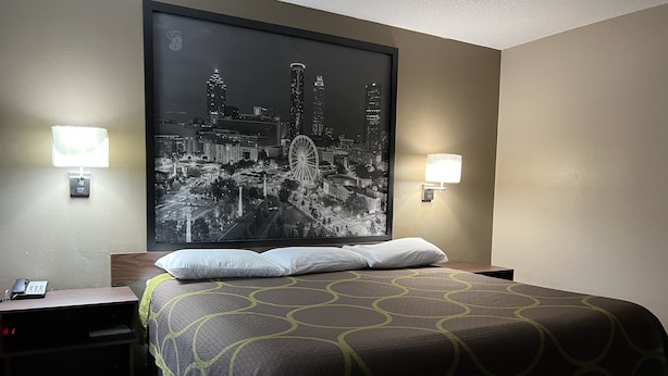 A hotel room with a large bed, two bedside lamps, a nightstand with a phone, and a cityscape artwork on the wall.