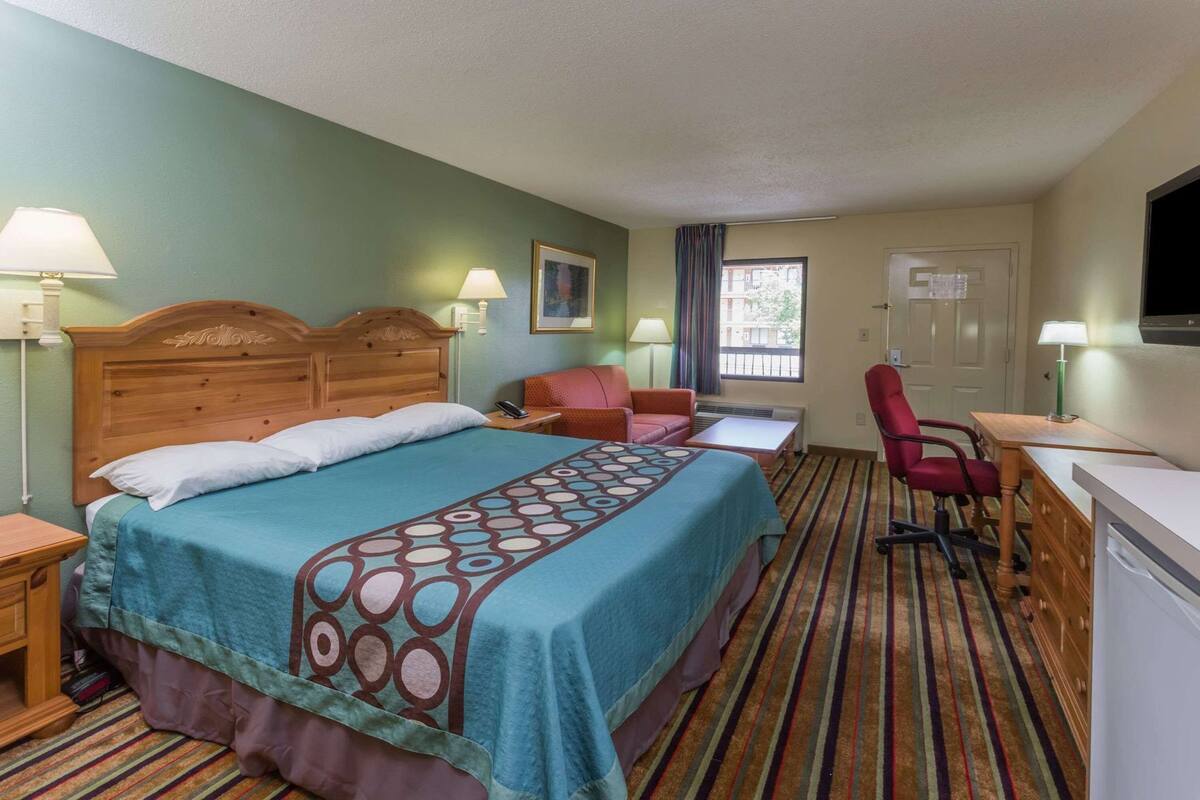 A hotel room with a large bed, a desk, a chair, a TV, and a window.