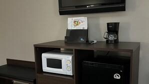 A hotel room with a flat-screen TV mounted on the wall, a microwave, a coffee maker, and a refrigerator.