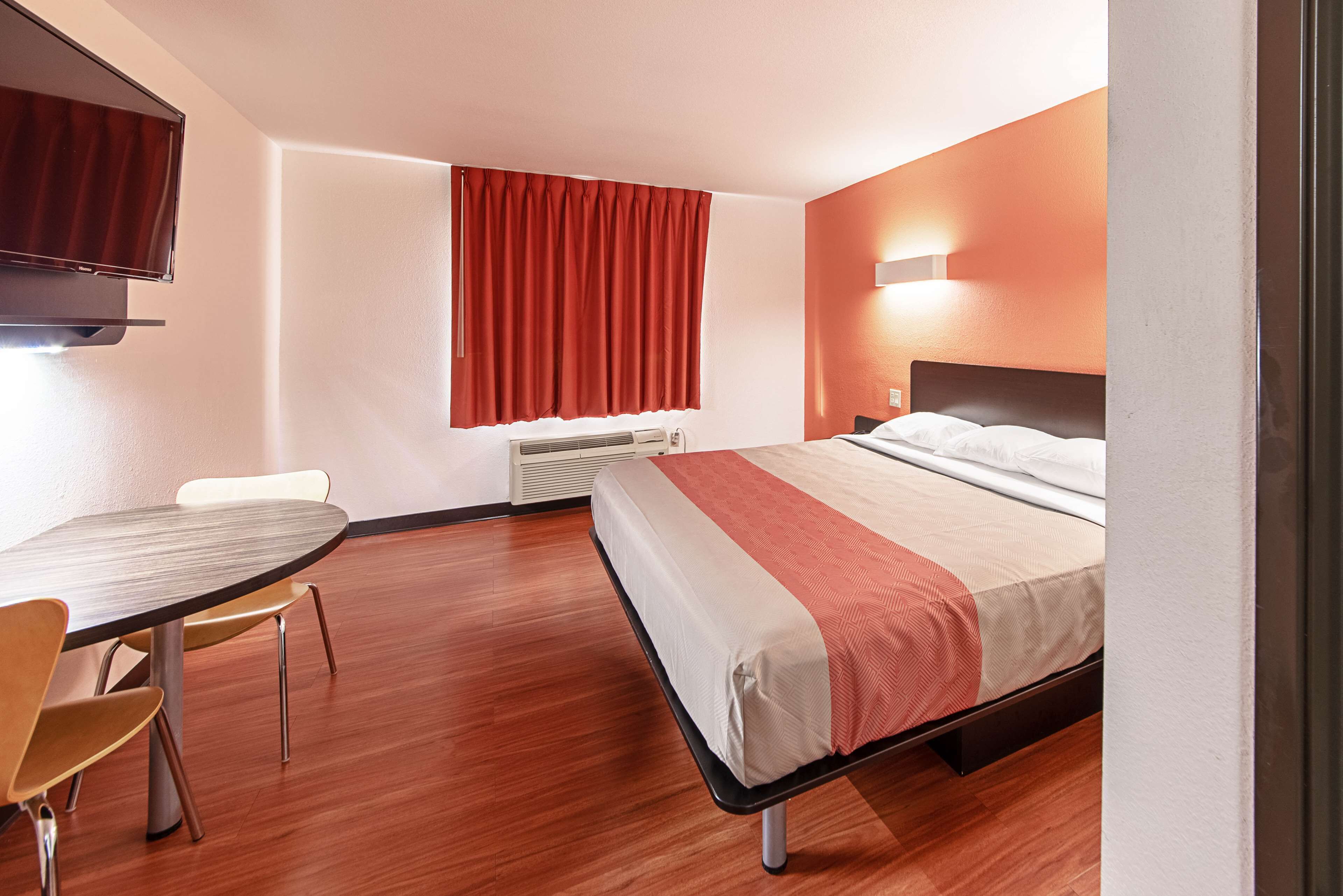 Habitació d'hotel amb llit, escriptori, cadira, televisió i finestra amb cortines.