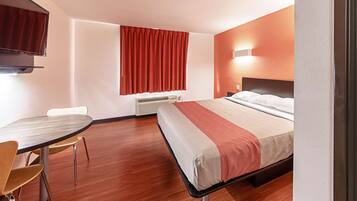 Habitació d'hotel amb llit, escriptori, cadira, televisió i finestra amb cortines.