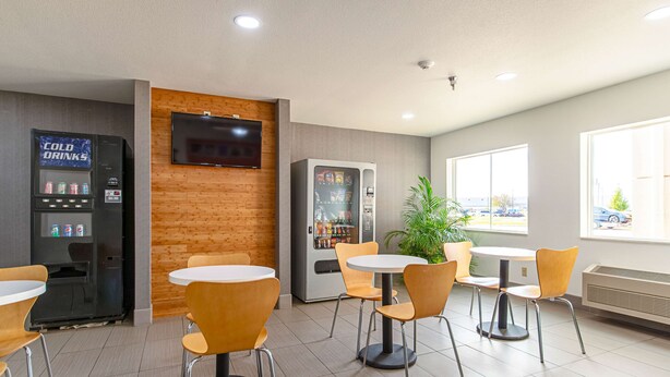 A modern indoor seating area with tables and chairs, a vending machine, and a television mounted on the wall. - Motel 6 Lebanon, IN (Lebanon)