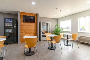 A modern indoor seating area with tables and chairs, a vending machine, and a television mounted on the wall. - Motel 6 Lebanon, IN (Lebanon)