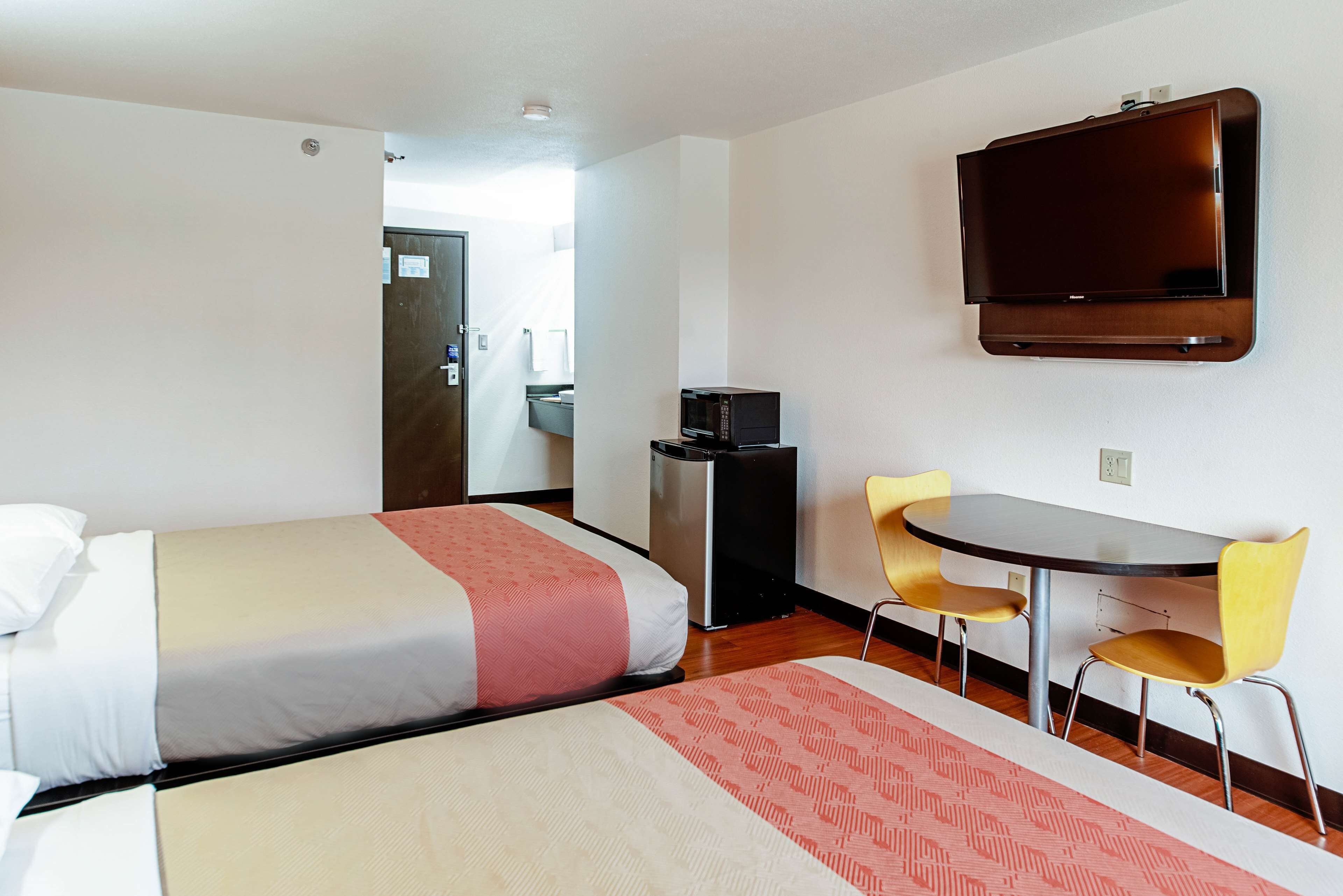 A hotel room with two beds, a desk with two chairs, a TV, and a microwave.