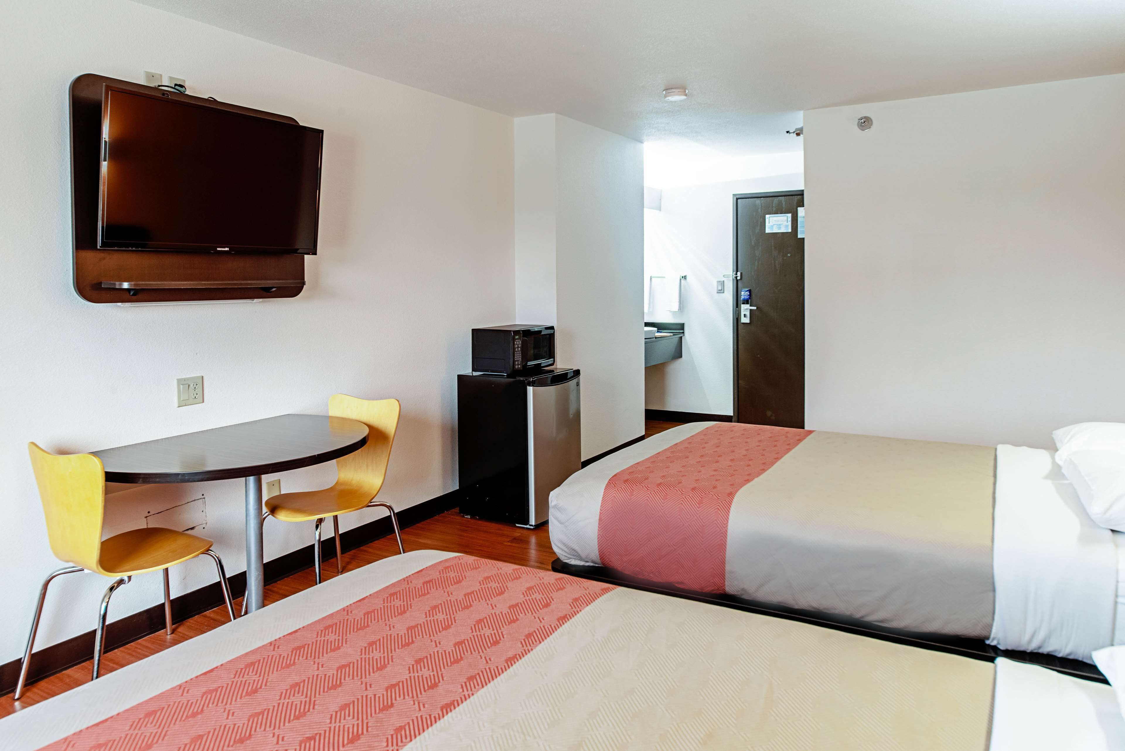 Una habitación de hotel con dos camas, un televisor montado en la pared, una mesita con sillas y un microondas.