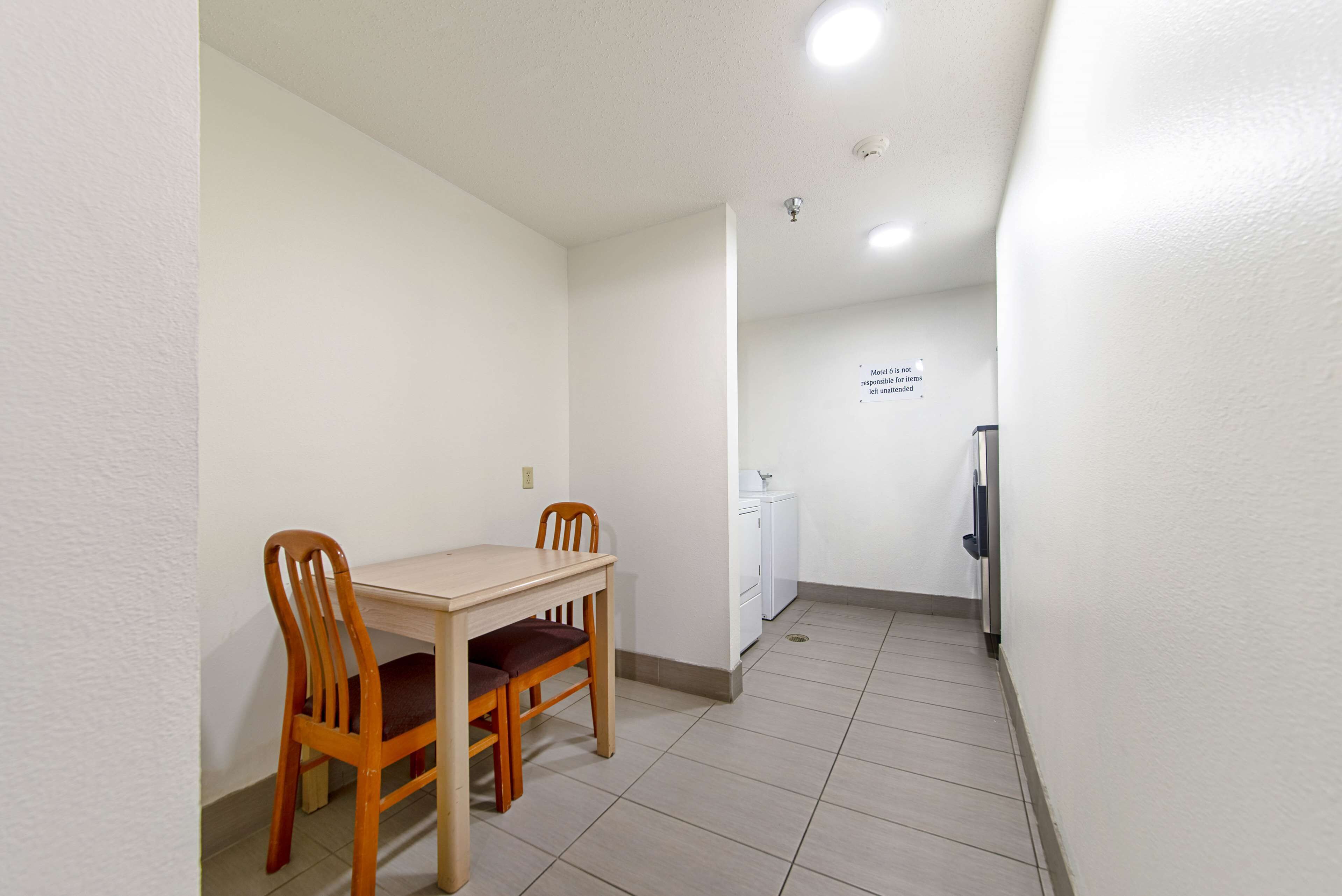 Una habitación pequeña y limpia con una mesa y sillas de madera, un refrigerador blanco y un lavamanos fijado a la pared.