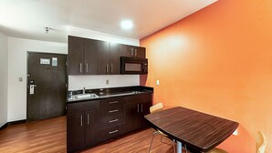 A compact kitchen with dark cabinets, a microwave, and a wooden table with a chair. - Motel 6 Lebanon, IN (Lebanon)