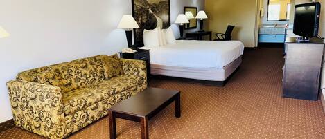 A hotel room with a bed, a sofa, a desk, and a television.