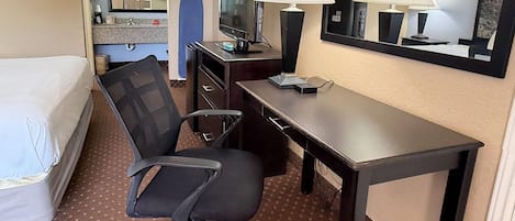 A hotel room with a bed, a desk, two lamps, a television, and a mirror.