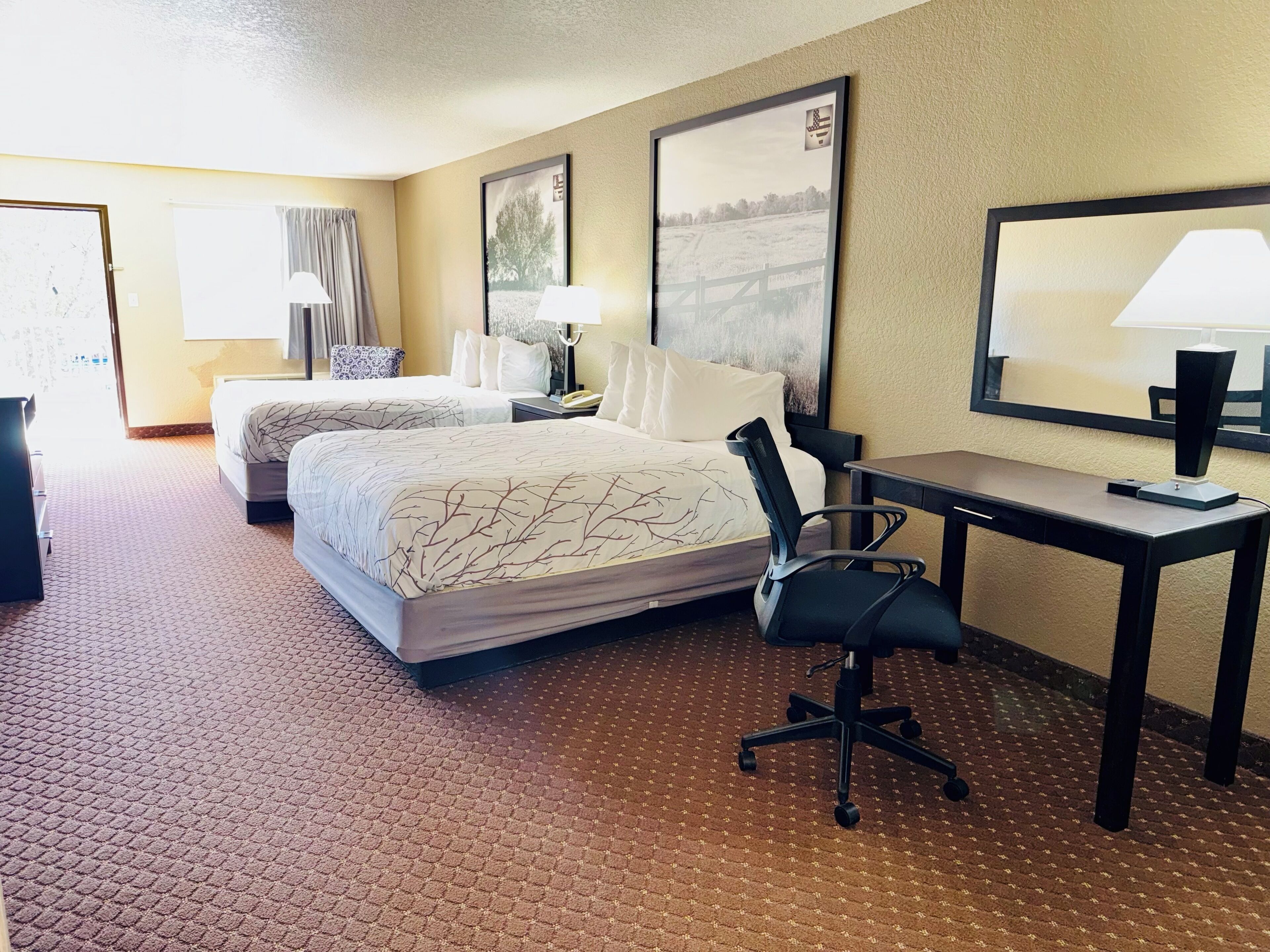 Une chambre d’hôtel avec deux lits, un bureau, une chaise et une grande fenêtre.