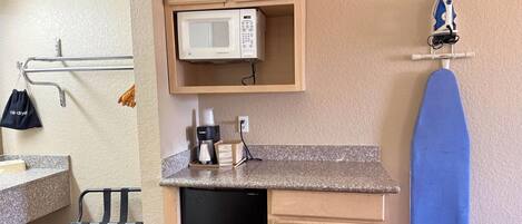 A kitchen with a microwave, ironing board, and a dish rack.