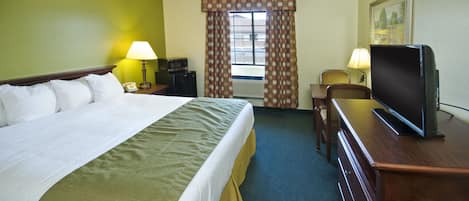 A hotel room with a bed, a desk with a television, a chair, a lamp, and a window with curtains.