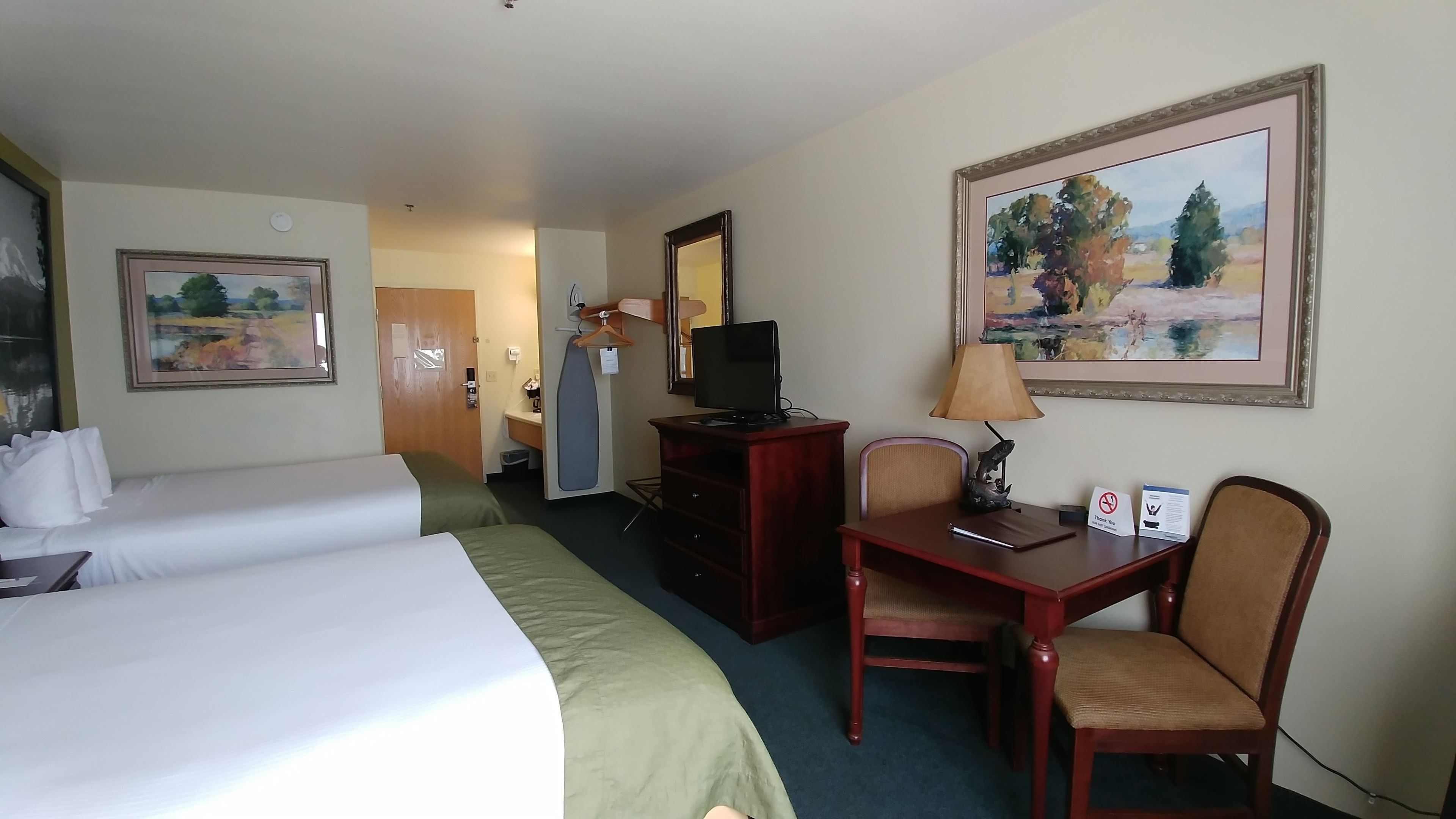 A hotel room with two single beds, a desk with a chair, a television, a lamp, and a painting on the wall.