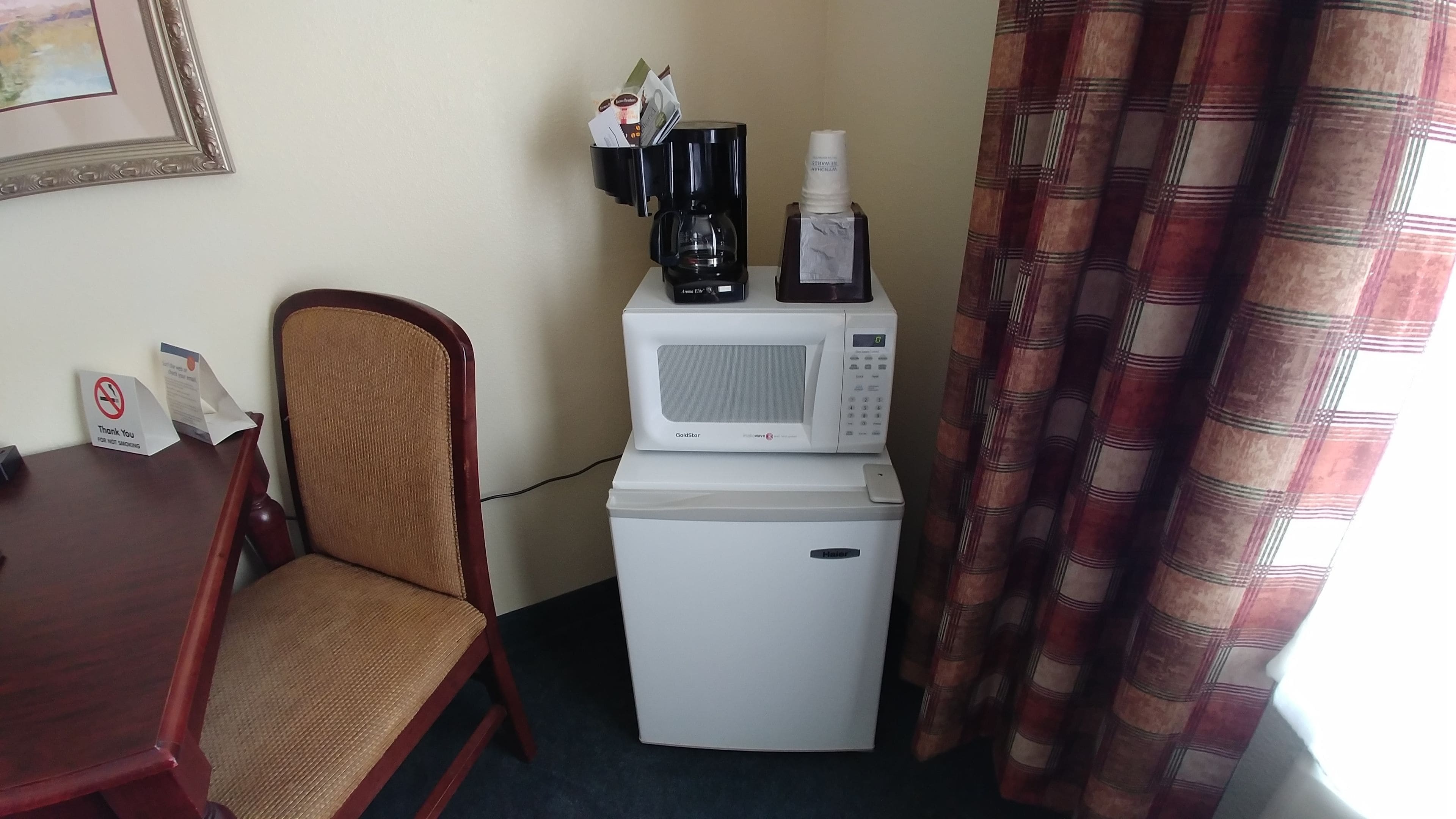 Une petite cuisine équipée d’un four à micro-ondes, d’une machine à café et d’un petit réfrigérateur. On y trouve une chaise et une table avec un panneau indiquant « Il est interdit de fumer ».