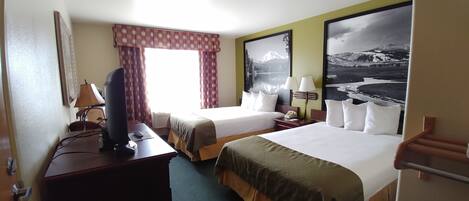 A hotel room with two beds, a desk with a computer, a telephone, and a window with a view of mountains.