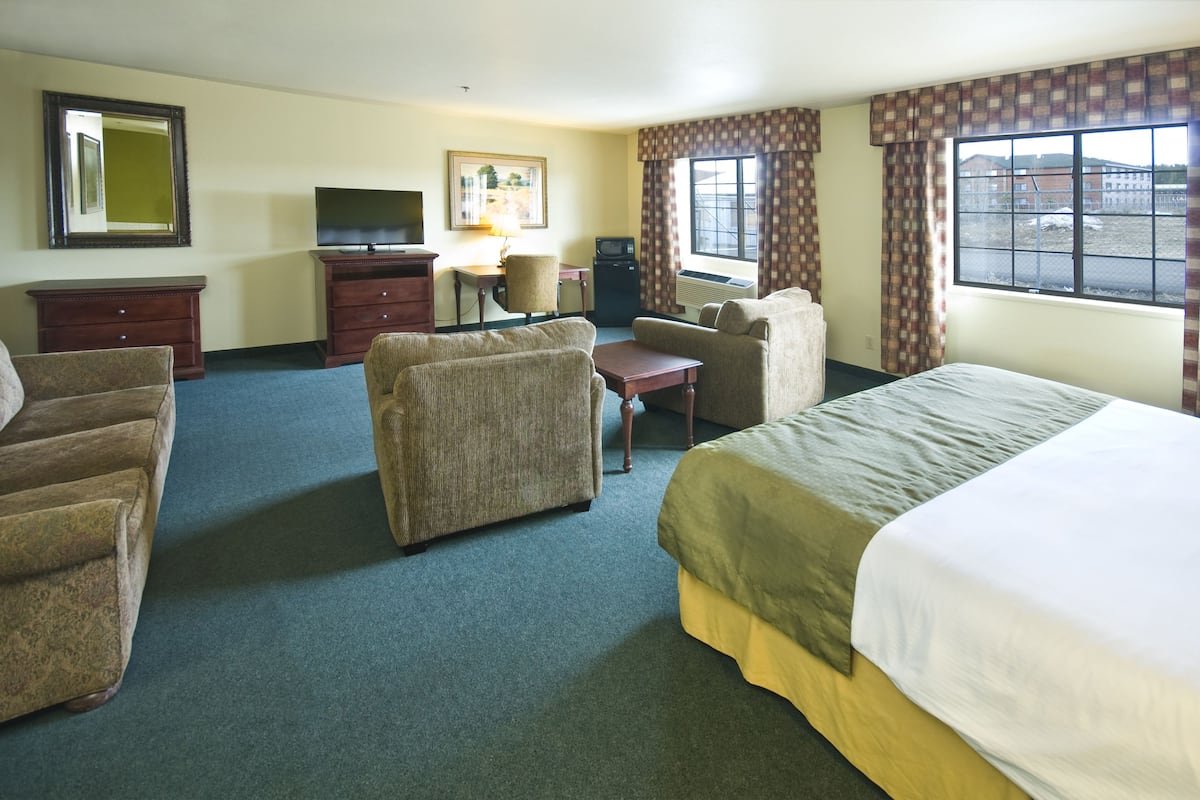 A hotel room with a bed, two armchairs, a sofa, a desk with a television, a chair, and a window with curtains.